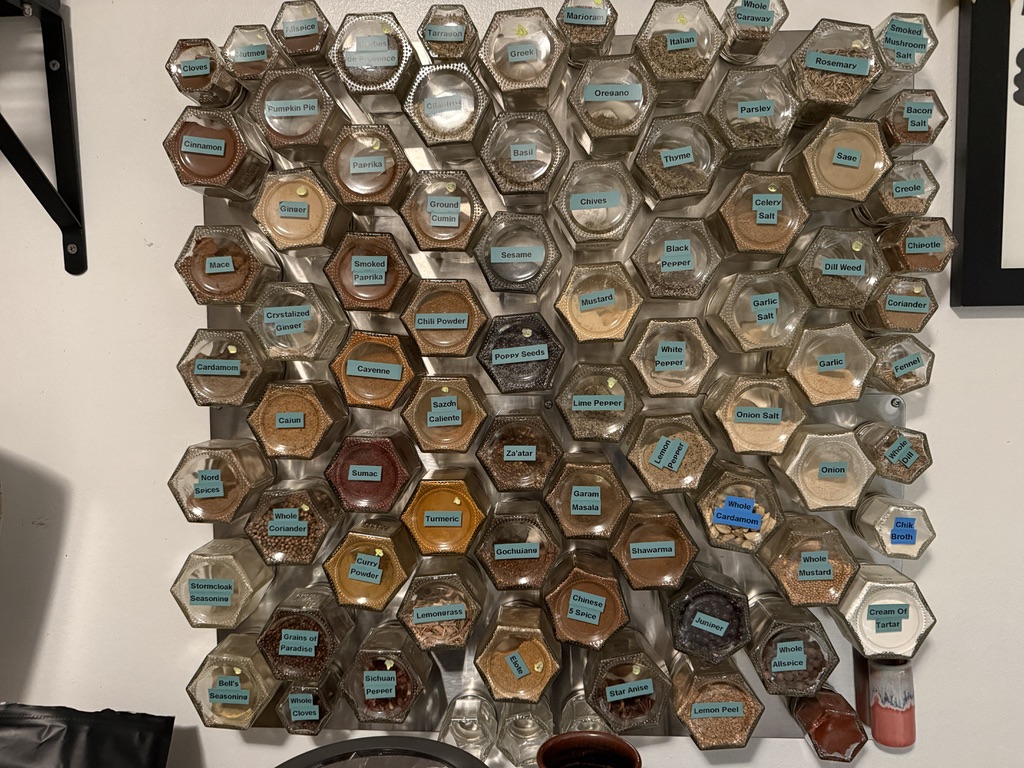 A wall covered with approximately 100 magnetic hexagonal glass spice jars arranged in a honeycomb pattern
