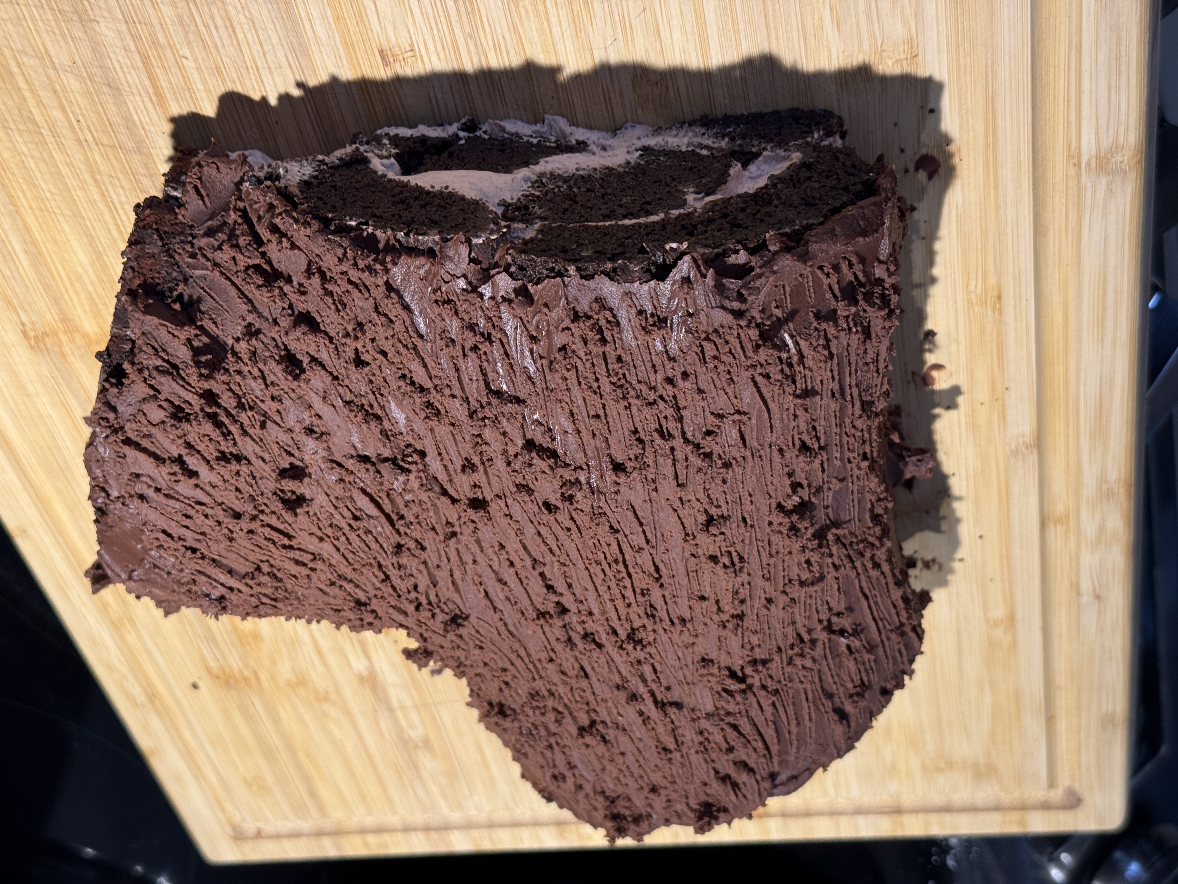 Chocolate yule log covered in ganache with fork-dragged bark texture, before decorations, showing the spiral of cake and cream at the cut end.