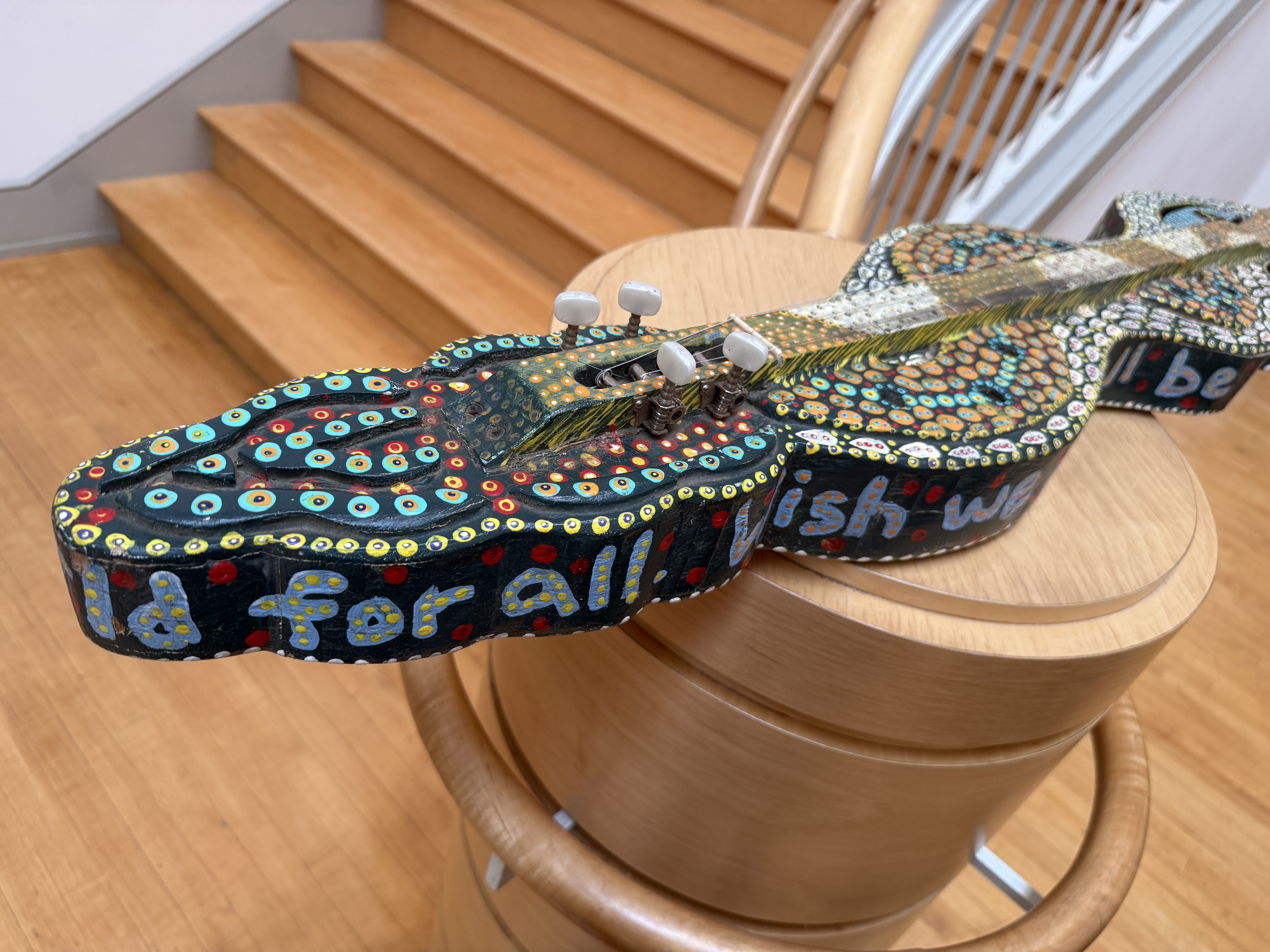 The snake dulcimer, painted with dense dot-work patterns and the words &ldquo;we could all be dazed&rdquo; along its body, displayed on a wooden pedestal